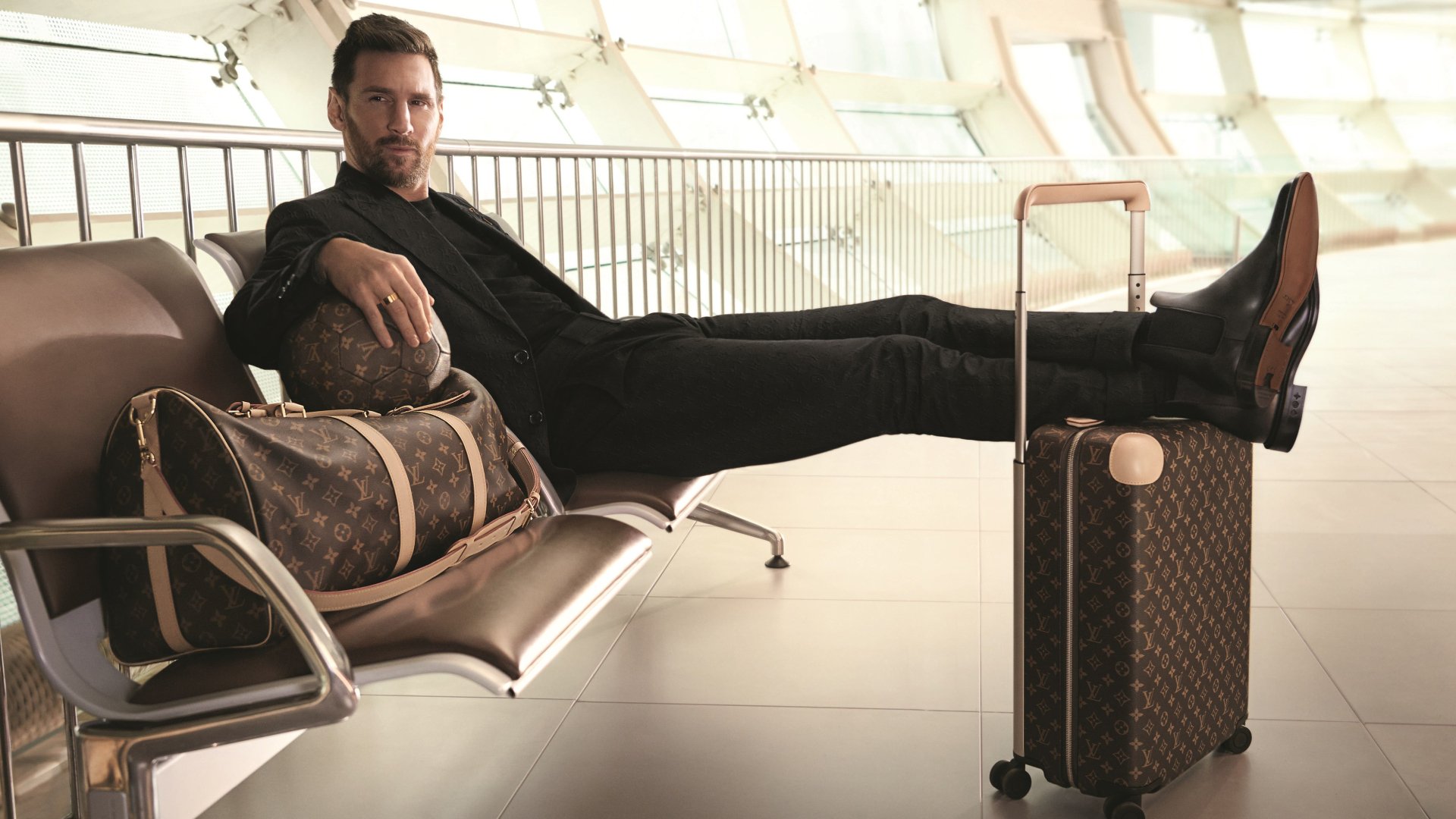 Lionel Messi lounges confidently on airport seating with luxury luggage in a sharp black outfit, captured in a 4K Ultra HD sports-themed PC desktop wallpaper.