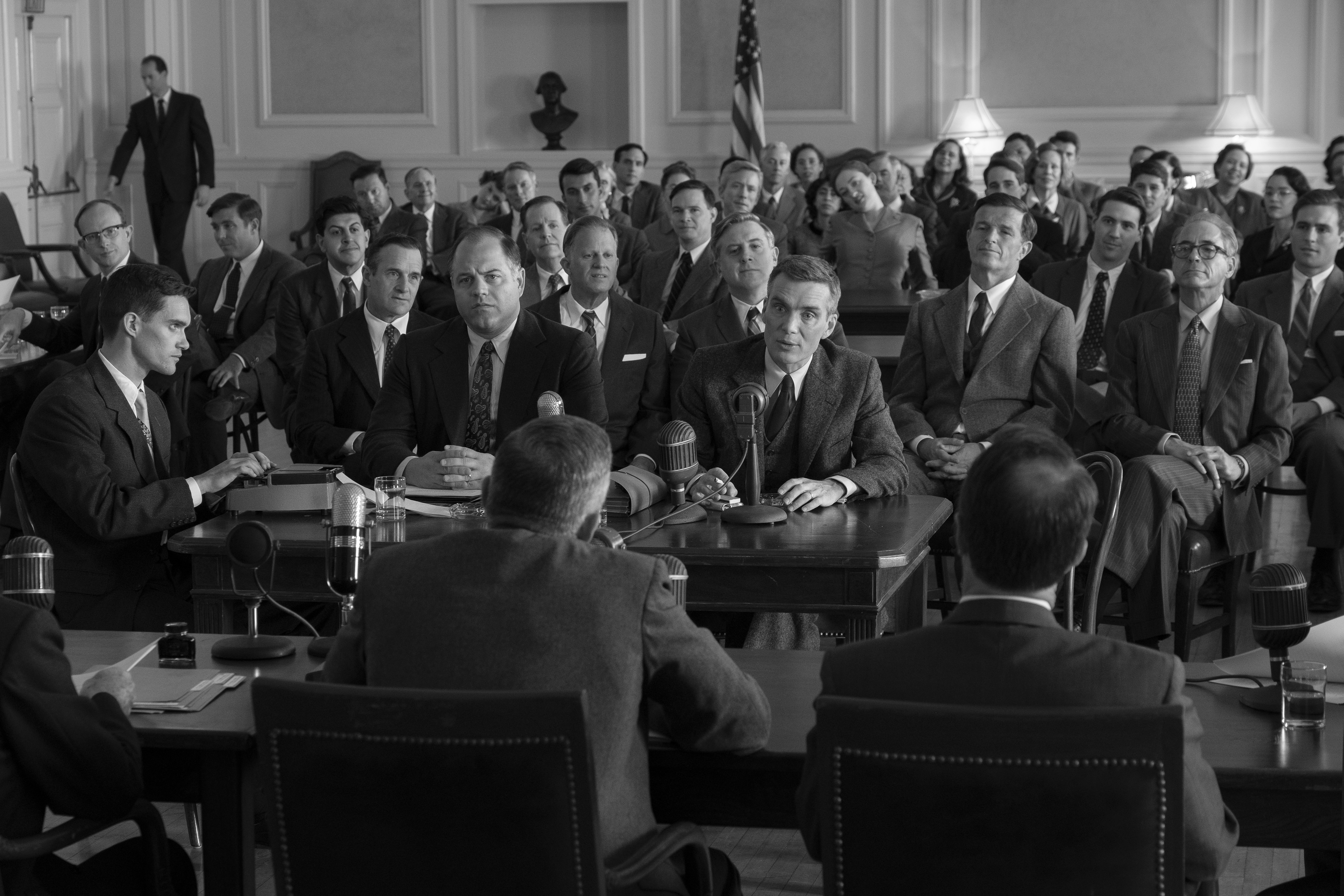 Black and white HD desktop wallpaper featuring a historical setting with a group of men in suits at what appears to be a government hearing, tagged with Oppenheimer.