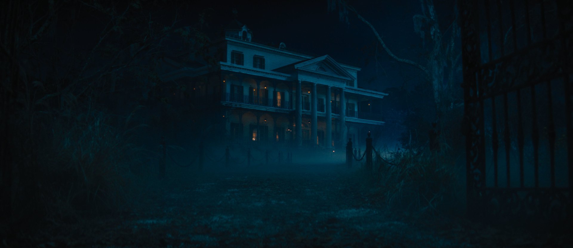 HD desktop wallpaper of a spooky, illuminated mansion in a foggy, eerie forest setting from the movie Haunted Mansion.