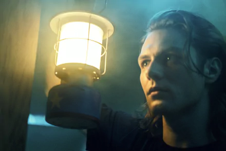 A dramatic scene from *Insidious: The Red Door*, featuring a character with long hair holding a lantern, set against a mysterious and atmospheric background.