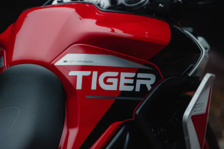 Close-up of the Triumph Tiger 900 GT Aragón motorcycle, showcasing its striking red and black design, featuring the bold TIGER badge. A dynamic HD desktop wallpaper.