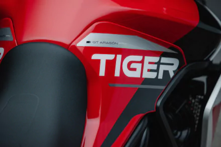 Close-up of the Triumph Tiger 900 GT Aragón motorcycle, showcasing its bold red design and distinctive TIGER branding. A striking HD desktop wallpaper for motorcycle enthusiasts.