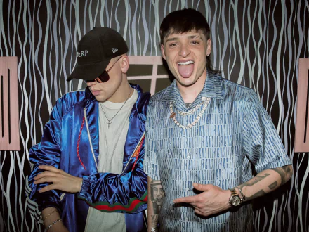 HD desktop wallpaper featuring Peso Pluma, with two men in stylish outfits posing in front of a striped backdrop.