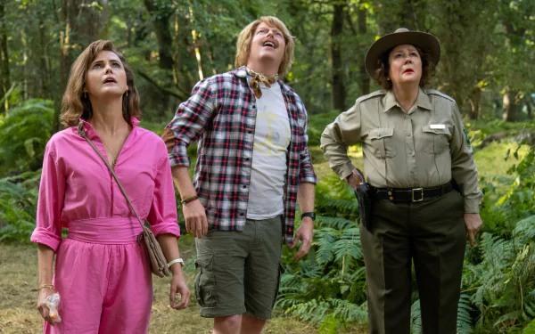 HD desktop wallpaper from 'Cocaine Bear' showcasing three characters gazing upwards with alarm in a forest setting.