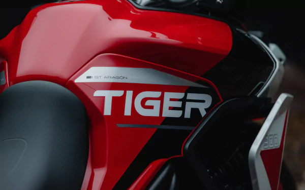 Close-up of the Triumph Tiger 900 GT Aragón motorcycle, showcasing its striking red and black design, featuring the bold TIGER badge. A dynamic HD desktop wallpaper.
