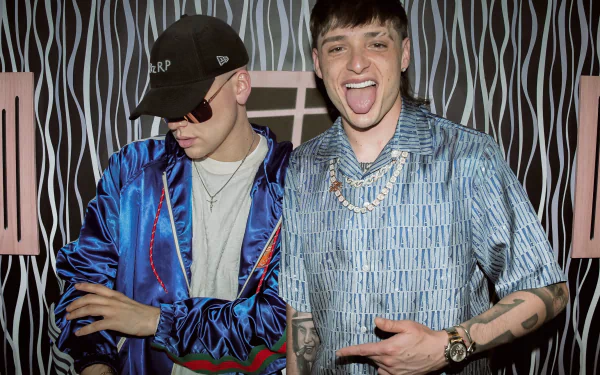 HD desktop wallpaper featuring Peso Pluma, with two men in stylish outfits posing in front of a striped backdrop.