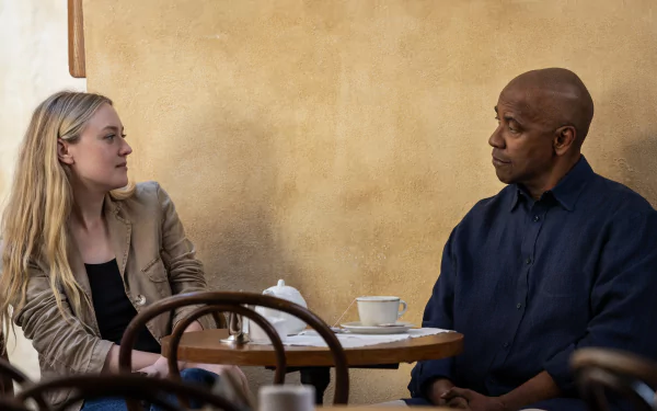 HD wallpaper featuring a tense scene from The Equalizer 3 with two key actors sitting at a café table, immersed in a deep conversation.
