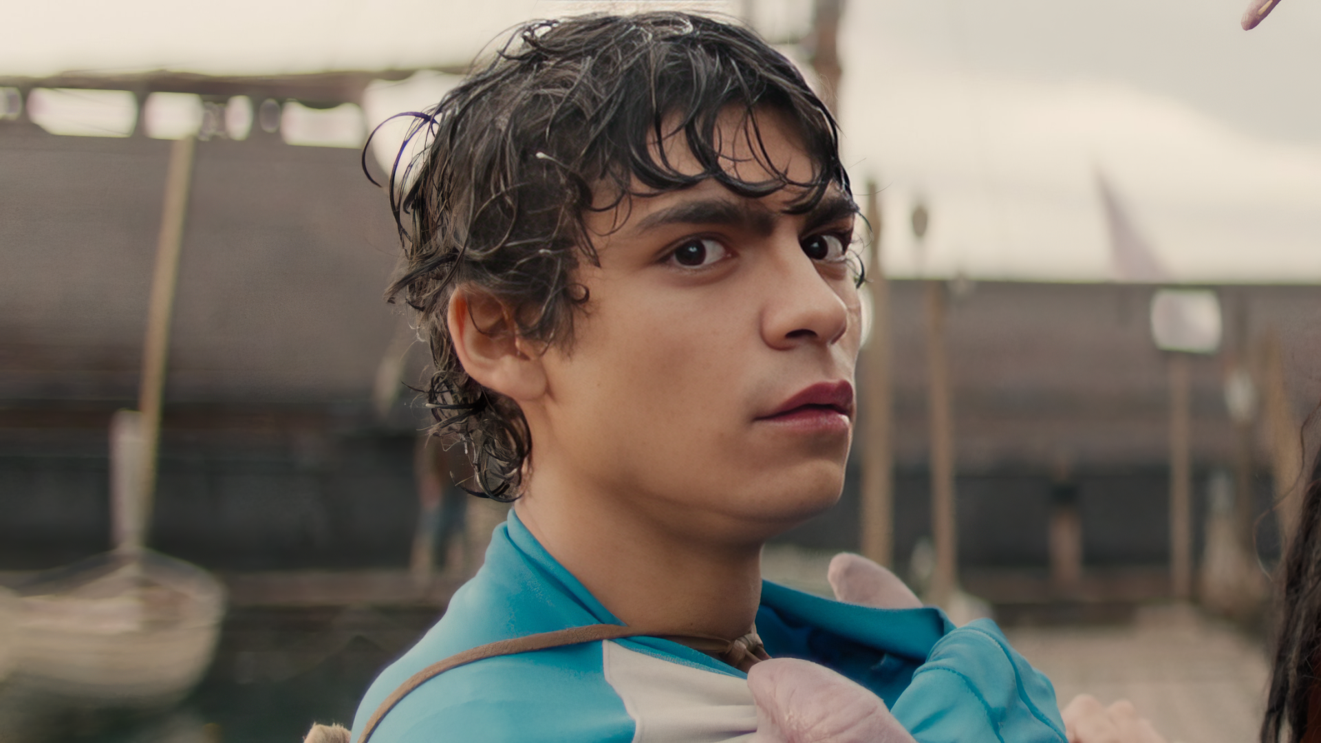 A close-up of a character from the live-action TV show One Piece, showcasing intense emotion against a backdrop of boats and a harbor setting. HD desktop wallpaper quality.