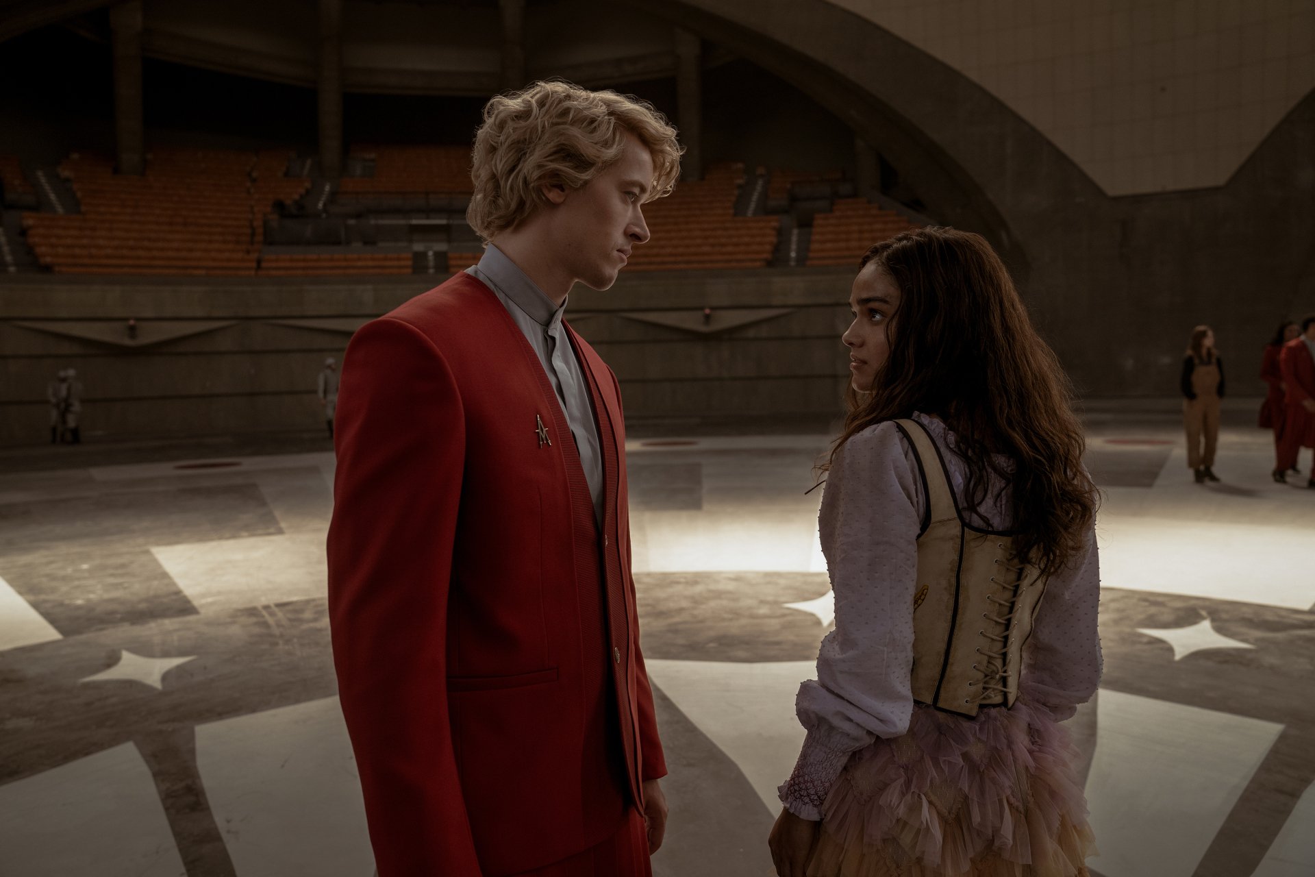 HD wallpaper featuring a scene from The Hunger Games: The Ballad of Songbirds & Snakes with two characters standing face-to-face in an arena setting.