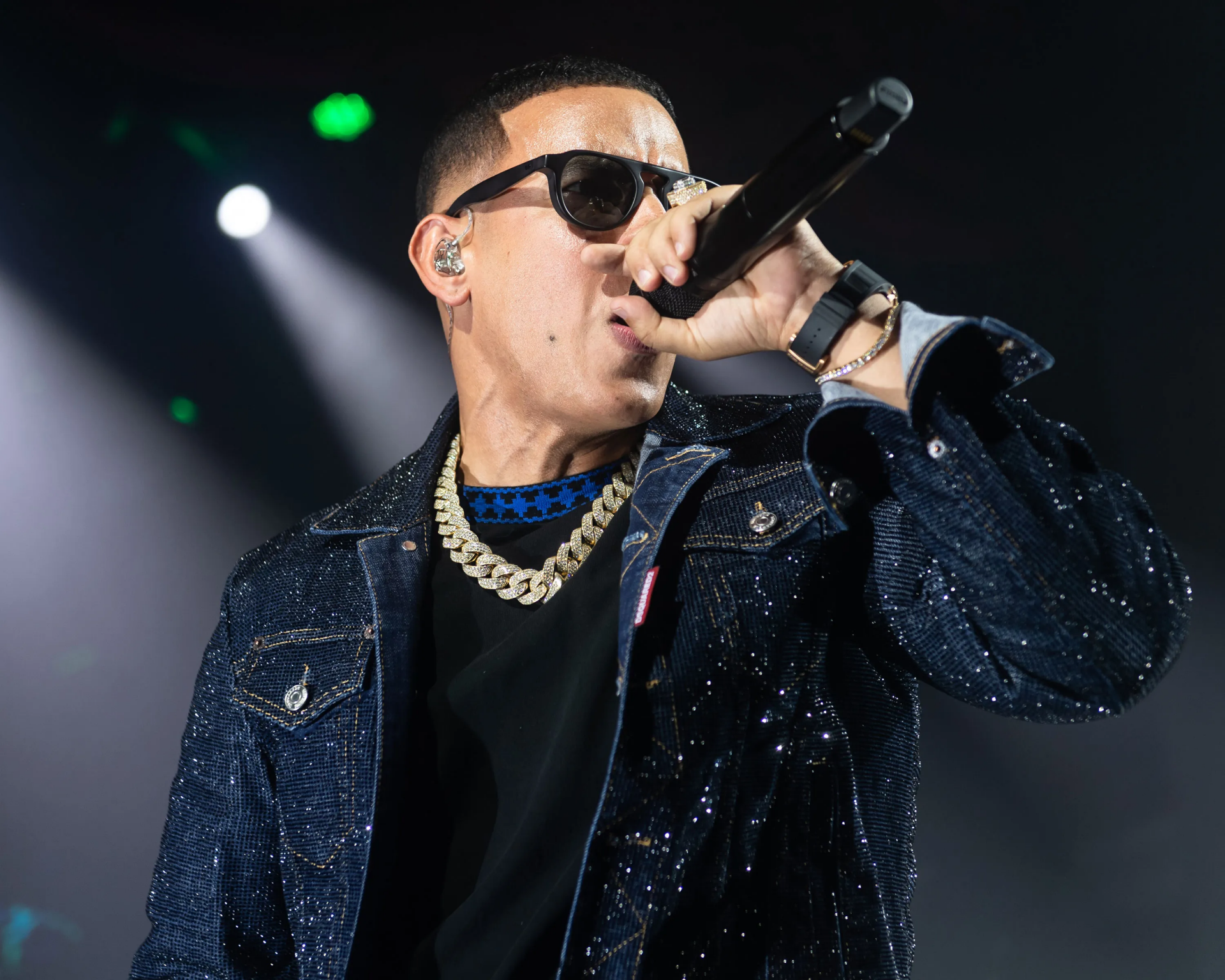 HD wallpaper of a performer in a glittering jacket singing into a microphone on stage, with bright stage lights in the background.