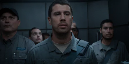 HD wallpaper featuring a scene from For All Mankind with a focused man in uniform foreground and fellow personnel in background.