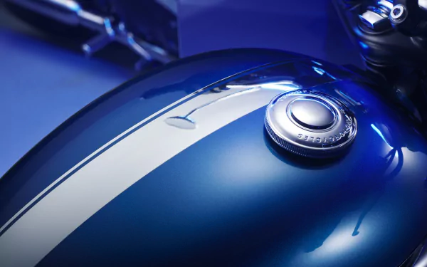 Close-up HD wallpaper of the chrome fuel tank on a Triumph Bonneville T100 in blue with elegant white stripes, showcasing the shiny chrome details and the iconic Triumph logo.