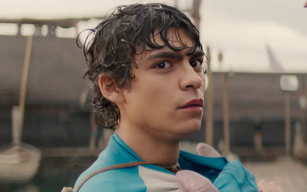 A close-up of a character from the live-action TV show One Piece, showcasing intense emotion against a backdrop of boats and a harbor setting. HD desktop wallpaper quality.