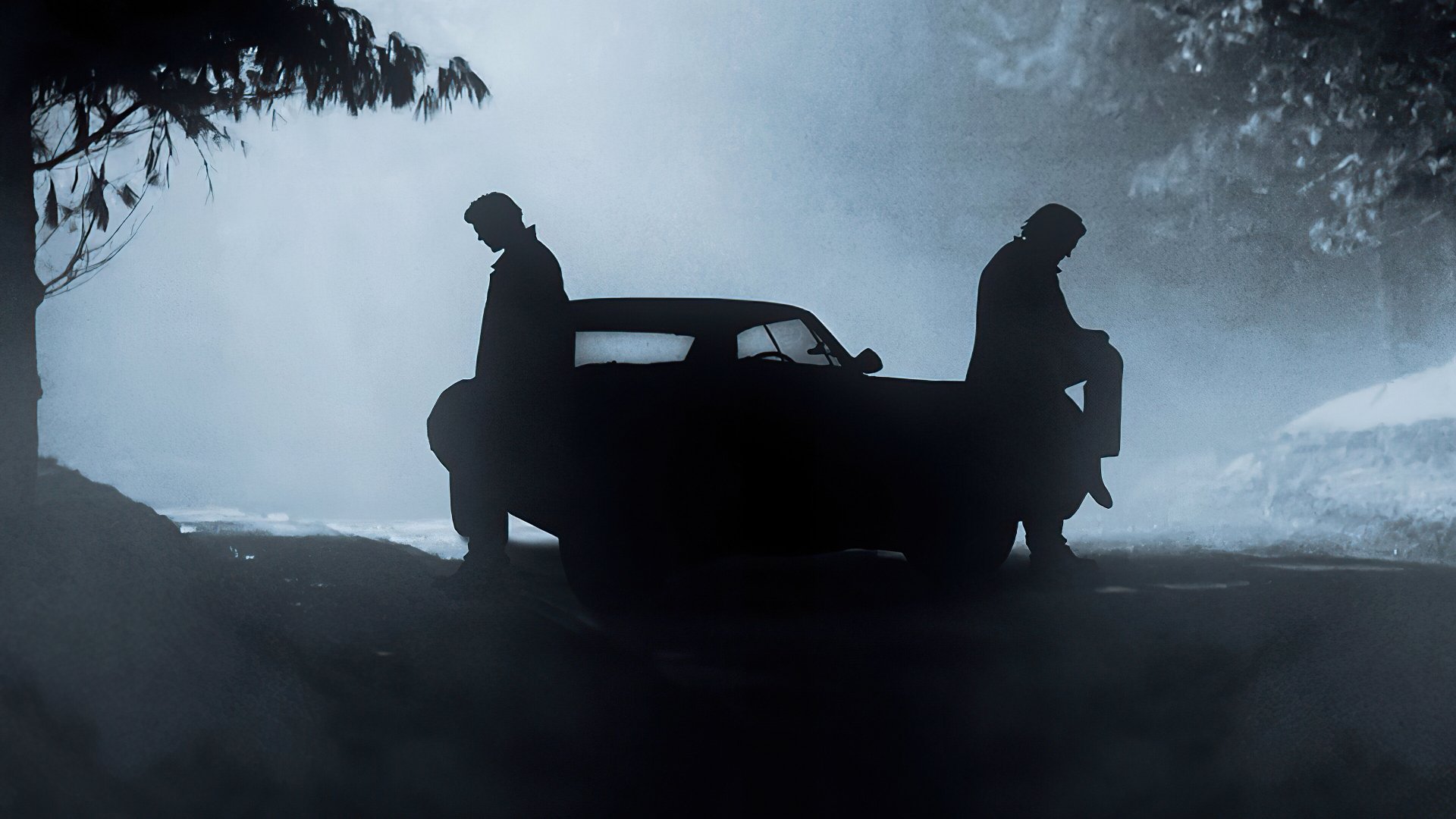 Silhouettes of Dean and Sam Winchester leaning against their car in a misty, dark setting from the TV show Supernatural, presented as a 4K Ultra HD desktop wallpaper.