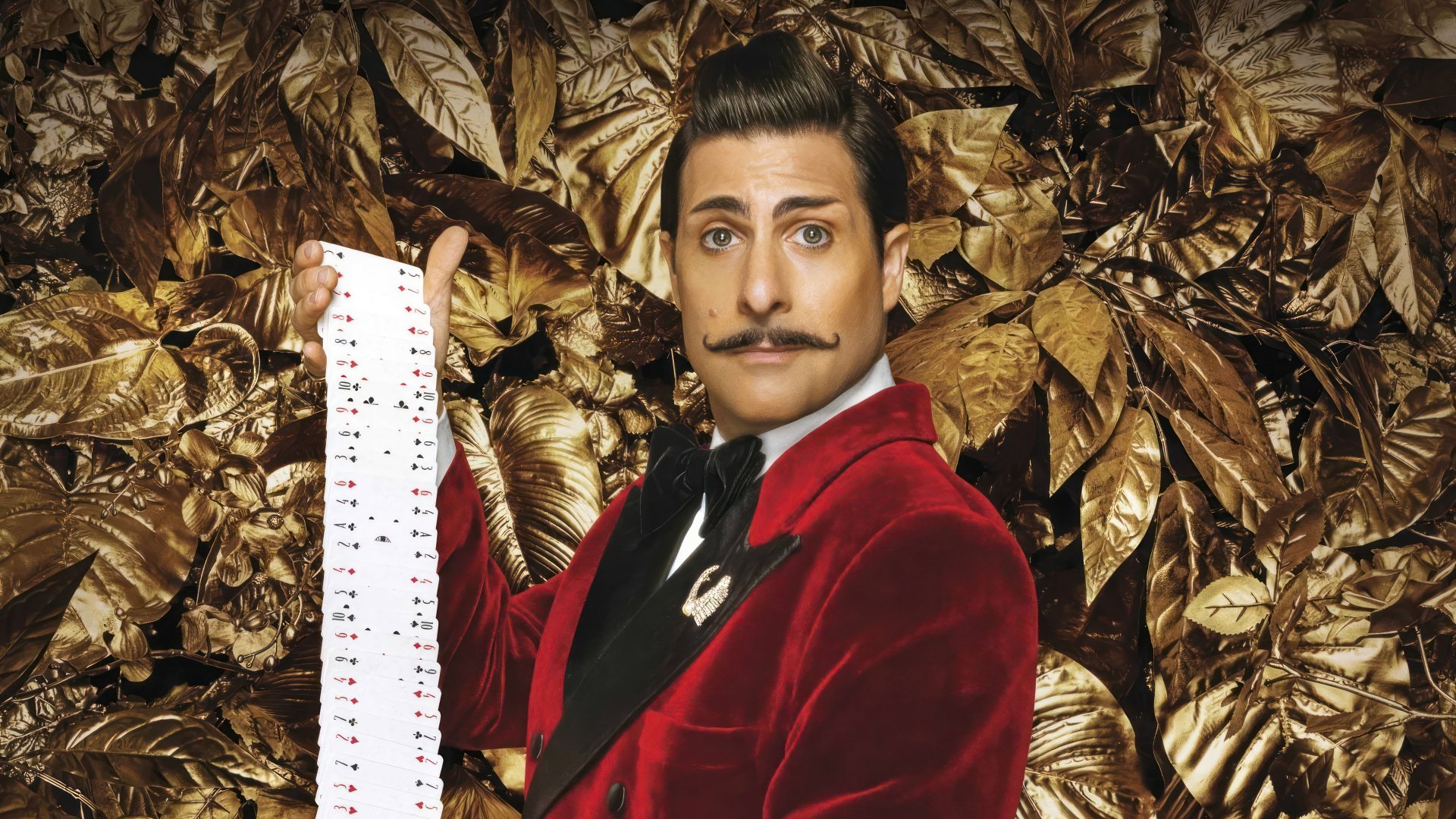 Promotional wallpaper for The Hunger Games: The Ballad of Songbirds & Snakes featuring a man in a red suit in front of a golden foliage background.