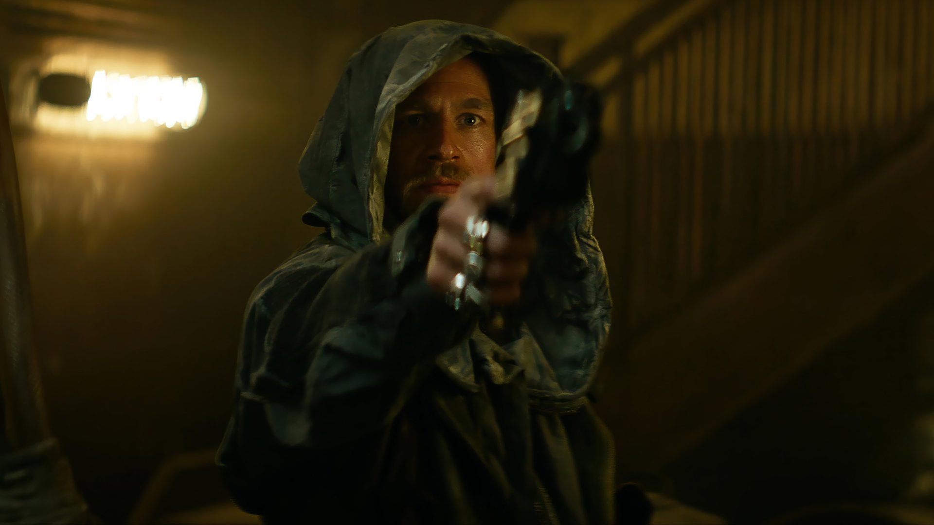 A dramatic scene from the movie Rebel Moon, featuring a character in a hooded cloak aiming a gun, set against a softly illuminated background. HD desktop wallpaper.