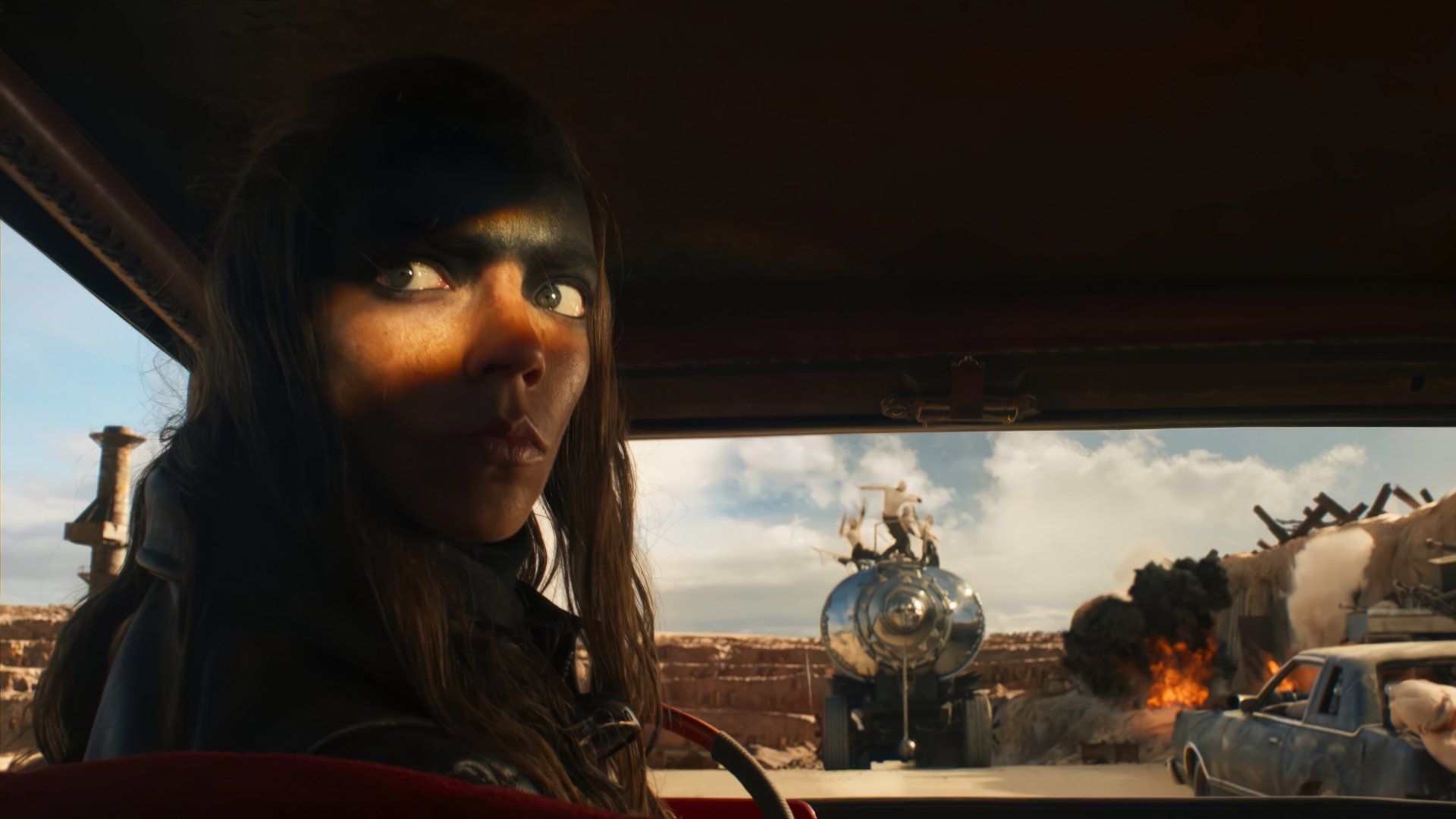 HD desktop wallpaper of Furiosa driving with explosive action scene from Furiosa: A Mad Max Saga in the background.