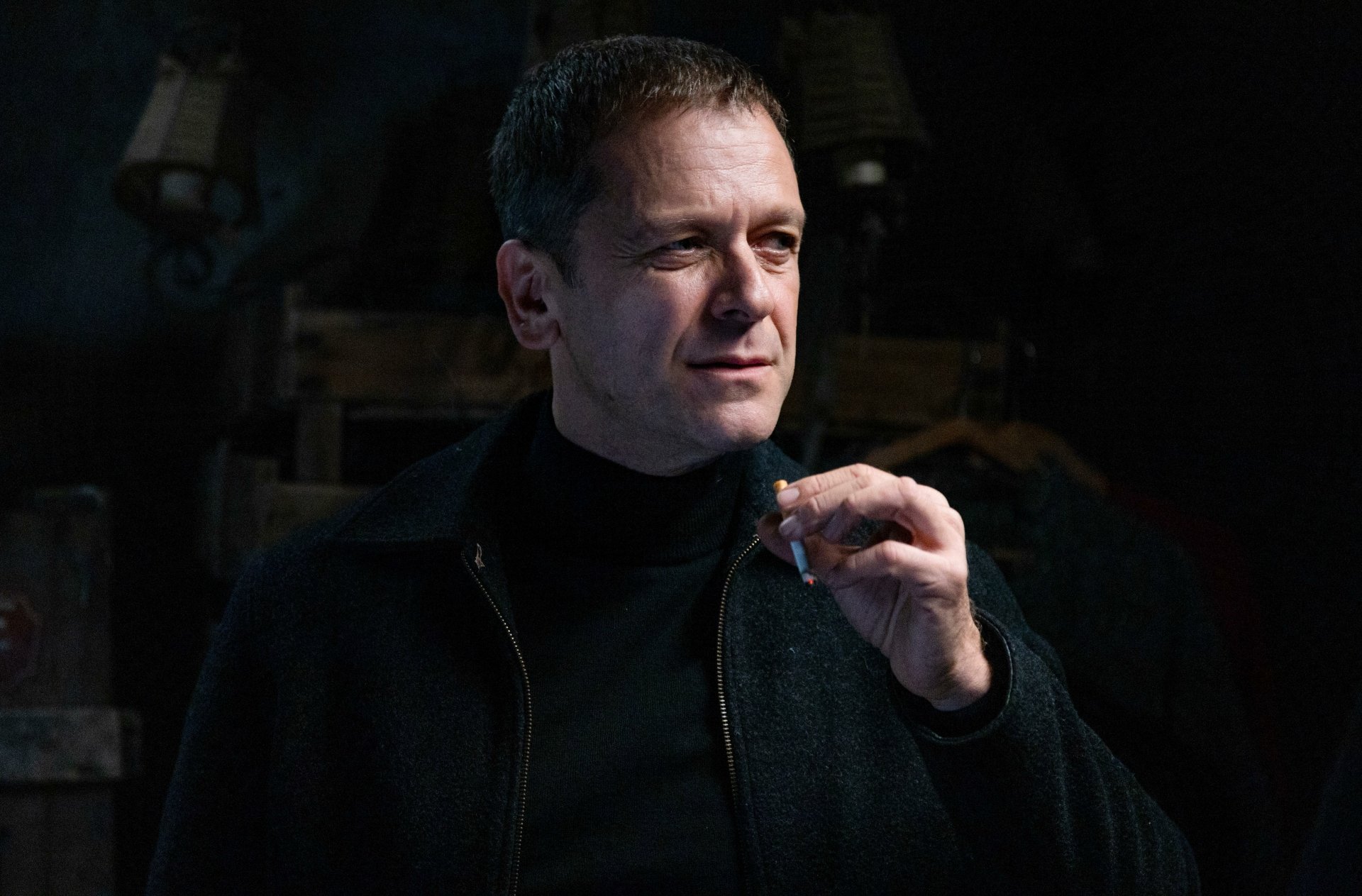 A moody close-up of a man holding a cigarette, exuding confidence and intrigue. This HD desktop wallpaper features a scene from the TV show Monsieur Spade.