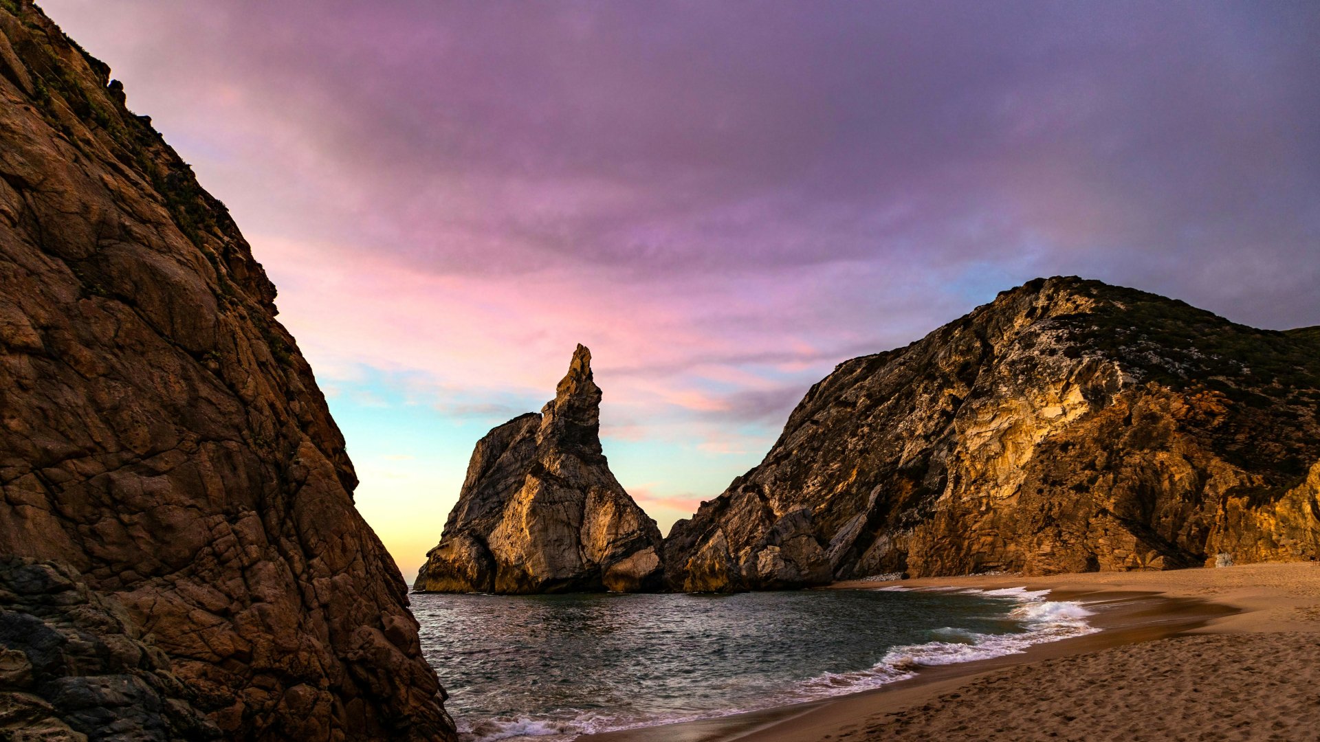 A tranquil beach scene at sunset with rocky cliffs and gentle waves, captured in stunning 4K Ultra HD for a vivid nature desktop wallpaper.