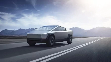 HD wallpaper of a Tesla Cybertruck driving on a road with mountains in the background.