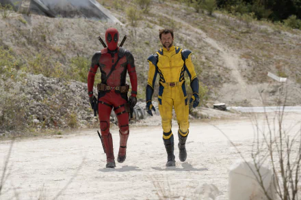 HD wallpaper of two characters from Deadpool 3, one in a red suit and the other in yellow, walking side by side on a dusty trail.
