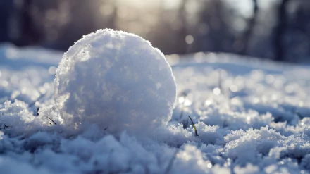 Close-up HD wallpaper of a snowball in fresh snow with sunlight filtering through, perfect for a desktop background.