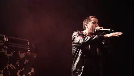 A dynamic HD desktop wallpaper featuring Canserbero passionately performing on stage, with a dramatic backdrop and engaging energy that captures the essence of music.