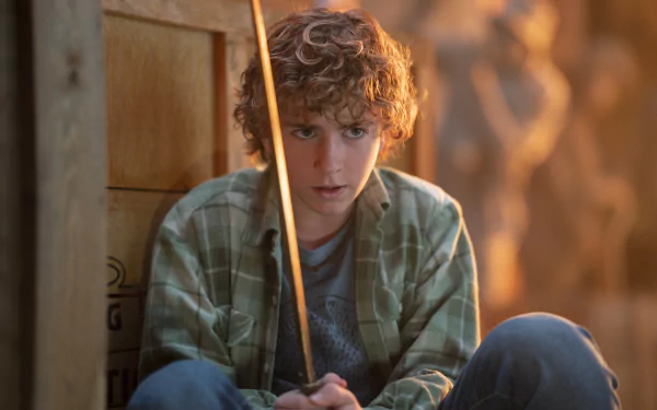 Young male character from the TV show Percy Jackson and the Olympians holding a wooden rod, looking thoughtful, in a high-definition desktop wallpaper.