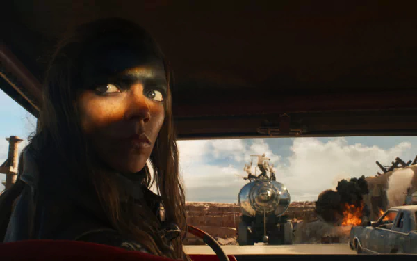 HD desktop wallpaper of Furiosa driving with explosive action scene from Furiosa: A Mad Max Saga in the background.