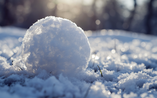 Close-up of a snowball on a snowy surface with sunlight filtering through in the background, ideal for HD winter-themed desktop wallpaper.