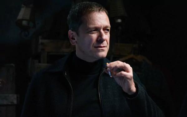 A moody close-up of a man holding a cigarette, exuding confidence and intrigue. This HD desktop wallpaper features a scene from the TV show Monsieur Spade.