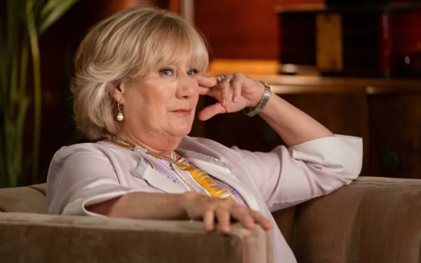 A thoughtful character from the TV show Death and Other Details sits on a couch, deep in contemplation, surrounded by a warm, inviting background.