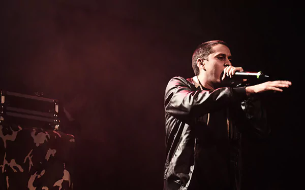 A dynamic HD desktop wallpaper featuring Canserbero passionately performing on stage, with a dramatic backdrop and engaging energy that captures the essence of music.