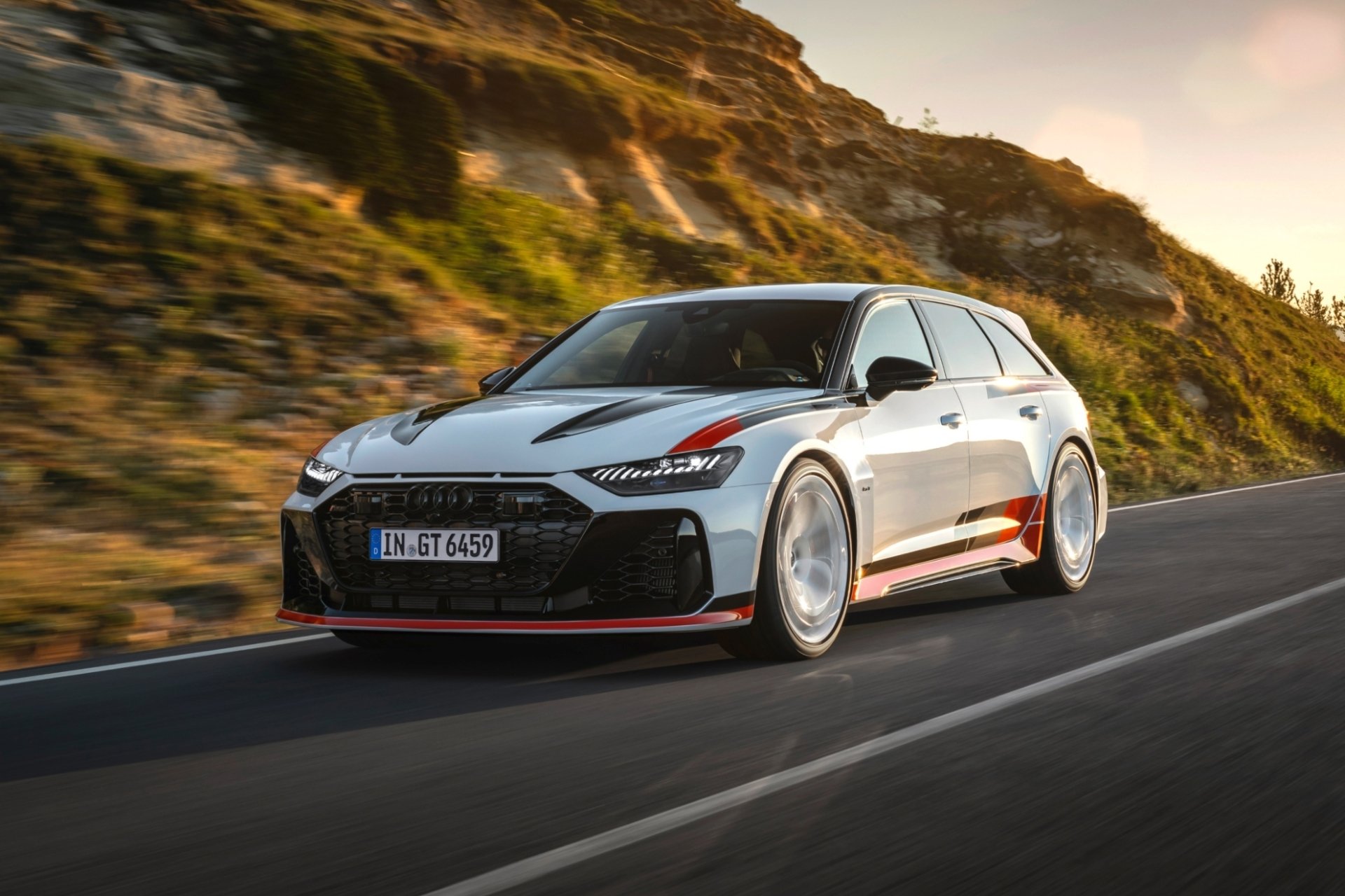 High-definition wallpaper featuring an Audi RS6 Avant GT racing along a scenic road, showcasing its sleek design and performance in motion against a dramatic backdrop.