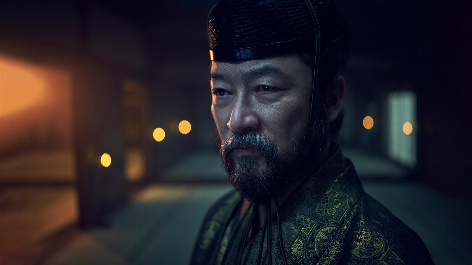 Close-up of a character in traditional attire from the TV Show Shogun (2024) with a dimly lit historical backdrop for an HD desktop wallpaper.