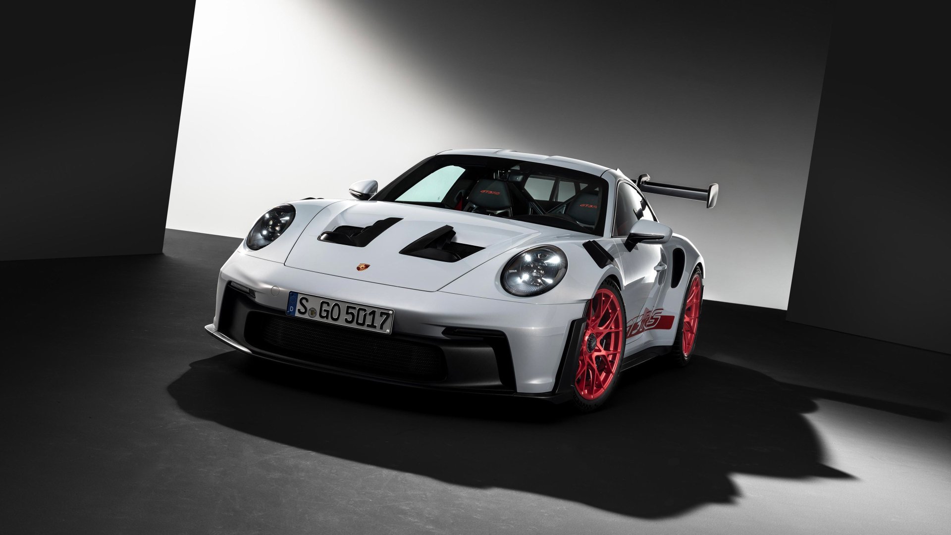 A striking Porsche 911 GT3 RS in white with bold red accents, set against a minimalistic background, showcasing its sleek design and performance-oriented features in high definition.
