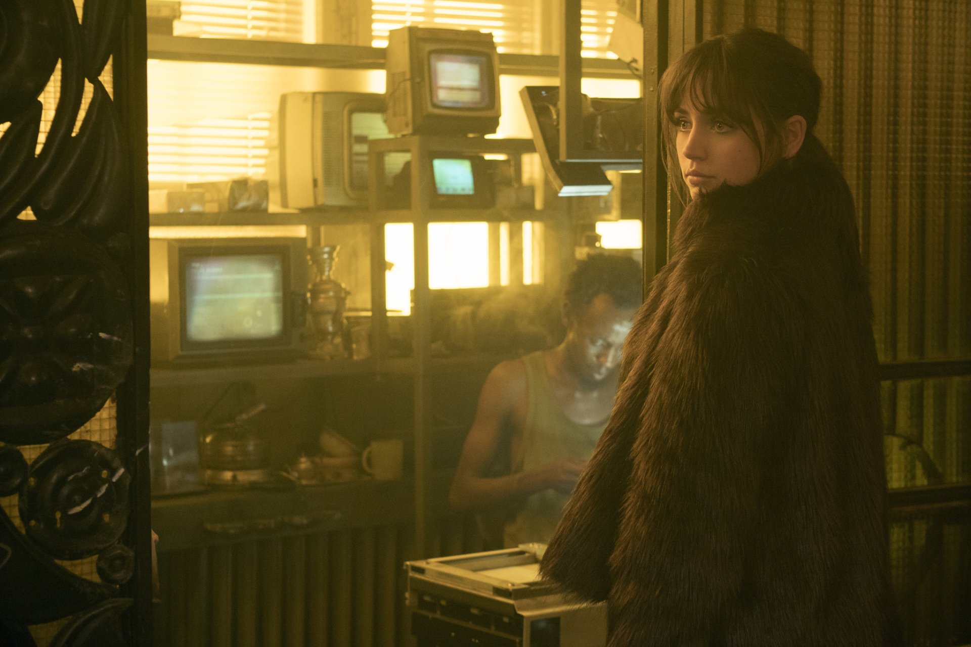 HD desktop wallpaper featuring a scene from Blade Runner 2049 with a character in a fur coat inside a dimly lit room with vintage monitors.