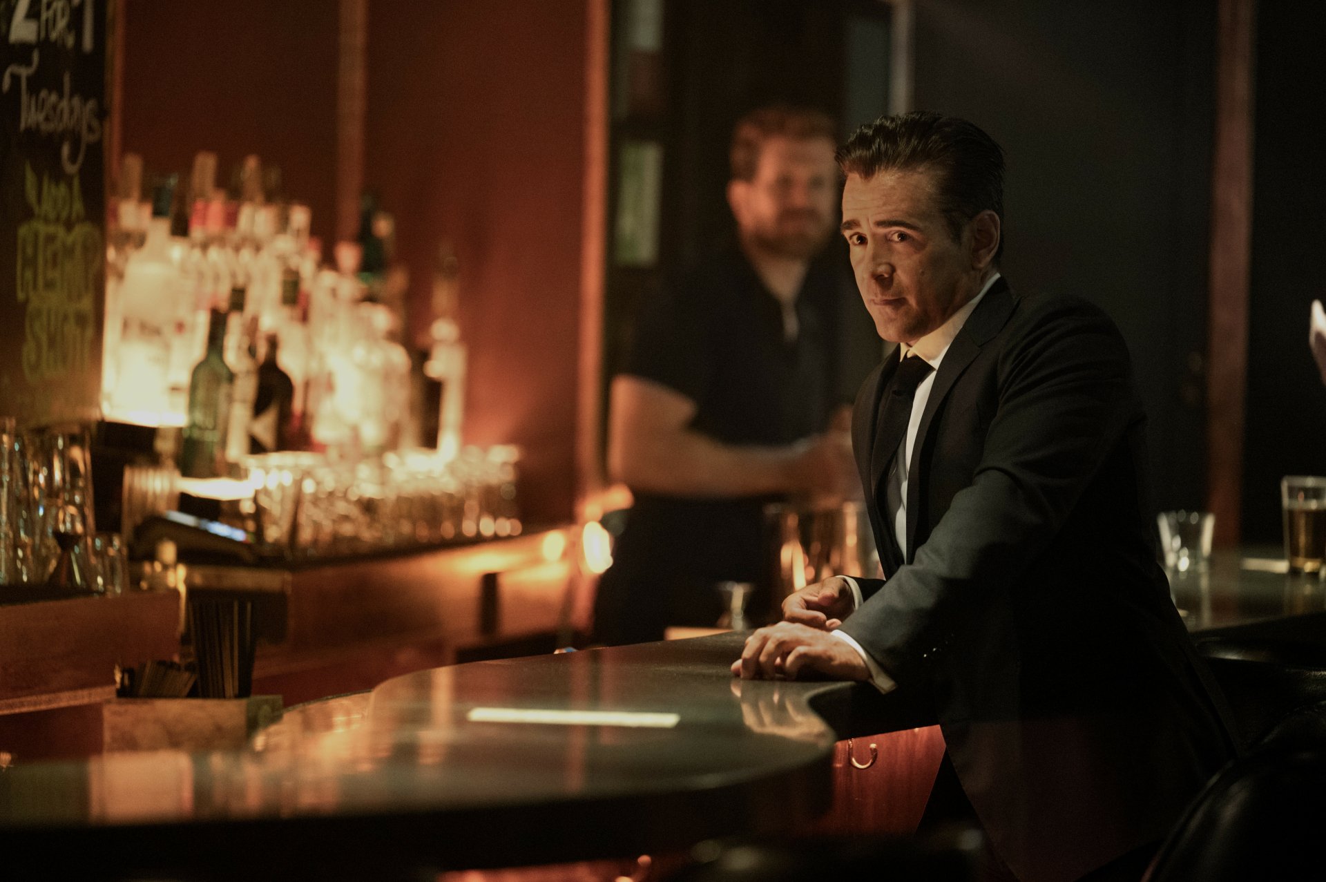 HD wallpaper featuring an intense scene from the TV show 'Sugar' (2024) set in a dimly lit bar with a male character in a suit sitting pensively.