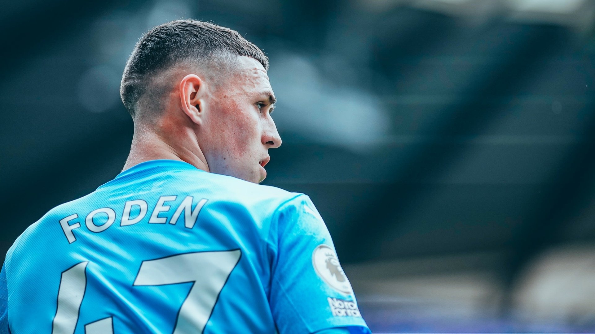 HD wallpaper of Phil Foden in Manchester City F.C. soccer kit, focused on the pitch.