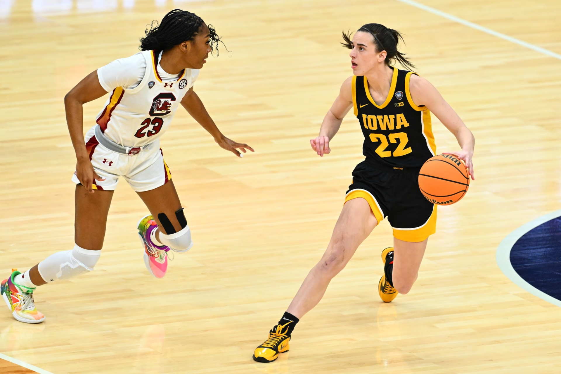 A basketball player in a yellow Iowa jersey with the number 22 dribbles past an opposing player during a game, in a high-definition desktop wallpaper.