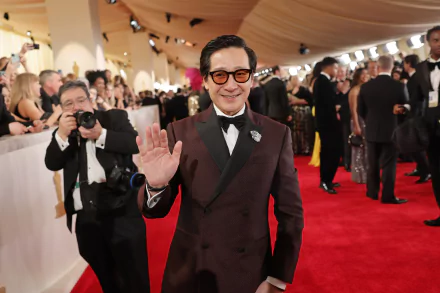 Ke Huy Quan smiling and waving on the red carpet at the Academy Awards, suited for a HD desktop wallpaper.
