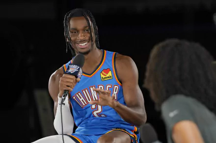 Shai Gilgeous-Alexander of the Oklahoma City Thunder smiles while speaking into a microphone, showcasing his dynamic presence in this vibrant HD background.