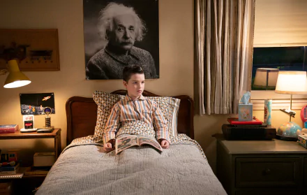 A scene from the TV show Young Sheldon, featuring a young boy sitting on his bed with a magazine, a poster of Einstein on the wall, and warm lighting creating a cozy atmosphere.