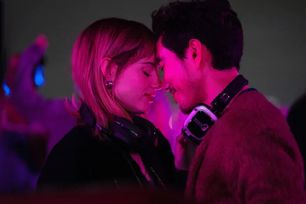 A romantic scene from the movie The Greatest Hits, featuring Lucy Boynton and Justin H. Min, set against vibrant neon lights, evoking a lively and intimate atmosphere.