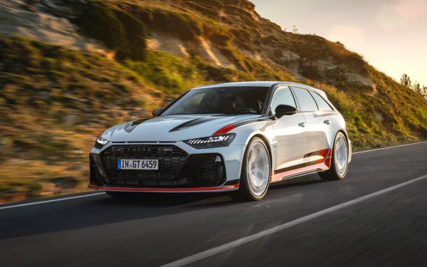 High-definition wallpaper featuring an Audi RS6 Avant GT racing along a scenic road, showcasing its sleek design and performance in motion against a dramatic backdrop.