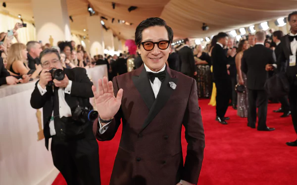 Ke Huy Quan smiling and waving on the red carpet at the Academy Awards, suited for a HD desktop wallpaper.
