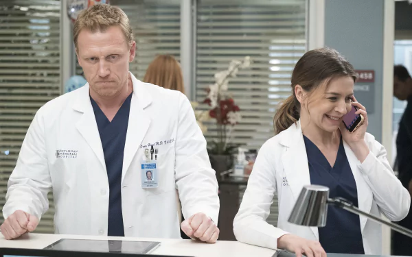 HD wallpaper featuring two doctors from the TV show Grey's Anatomy smiling and standing at a reception desk.