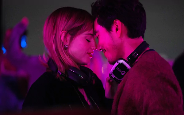 A romantic scene from the movie The Greatest Hits, featuring Lucy Boynton and Justin H. Min, set against vibrant neon lights, evoking a lively and intimate atmosphere.
