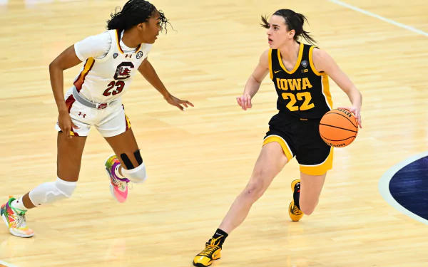 A basketball player in a yellow Iowa jersey with the number 22 dribbles past an opposing player during a game, in a high-definition desktop wallpaper.