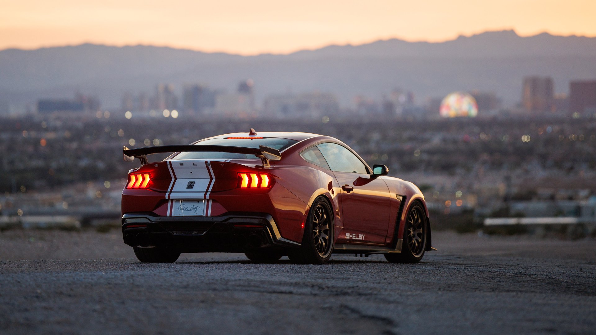 HD wallpaper of a Shelby Super Snake muscle car overlooking a cityscape at dusk.